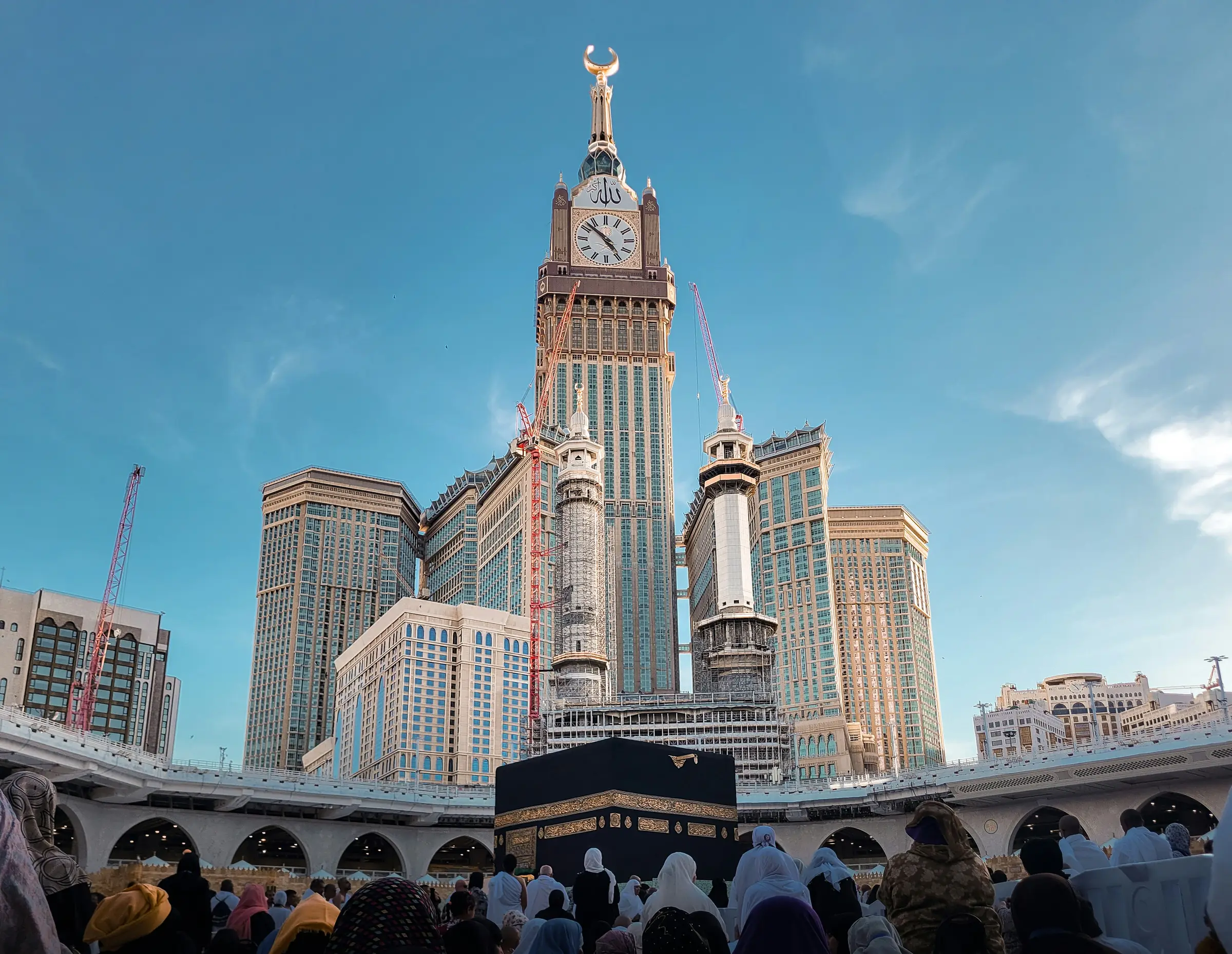 Pilgrims gathered before the Kaaba at Masjid al-Haram, with the Makkah clock tower rising behind