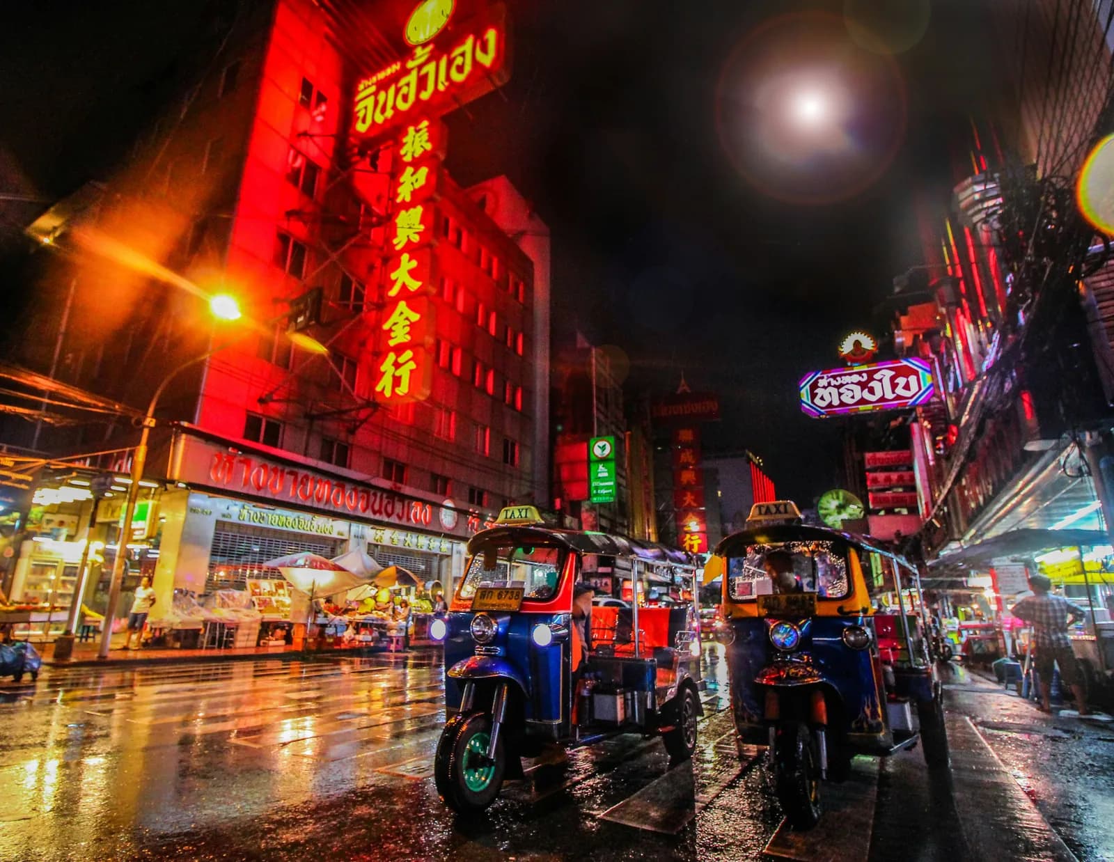 Tuk-tuks beneath neon signs on a rainy night in Bangkok’s Chinatown